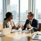 Business professionals wearing modern smart glasses having office discussion with laptops and city skyline background